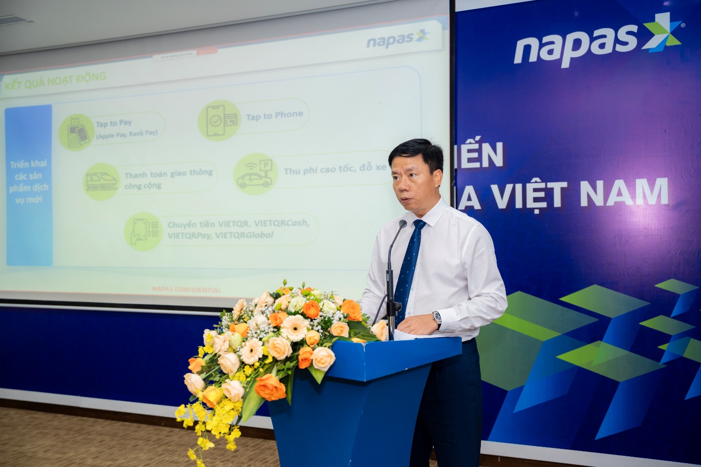 NAPAS tổ chức Hội nghị tuyên dương điển hình tiên tiến lần thứ II - Ảnh 3. A person standing at a podium with flowers AI-generated content may be incorrect.