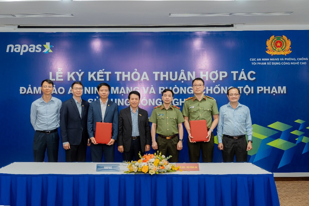 NAPAS and A05 Department (Ministry of Public Security) Sign Strategic Cooperation Agreement on Cybersecurity and High-Tech Crime Prevention- Ảnh 1. A group of men standing in front of a table with flowers AI-generated content may be incorrect.