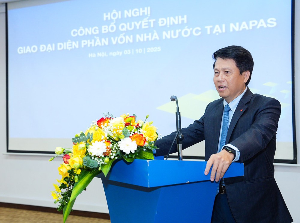 Hội nghị công bố và trao Quyết định giao đại diện phần vốn nhà nước tại NAPAS- Ảnh 1. A person standing at a podium with flowers AI-generated content may be incorrect.